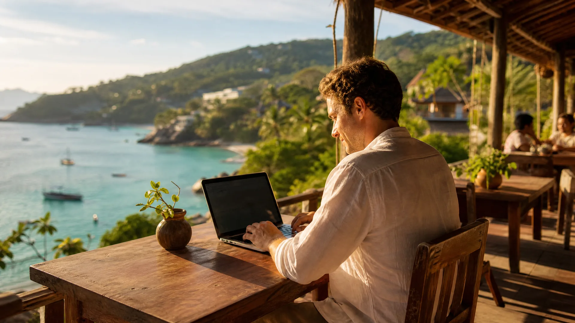 Digital Nomad arbeitet am Laptop mit Blick auf eine tropische Bucht