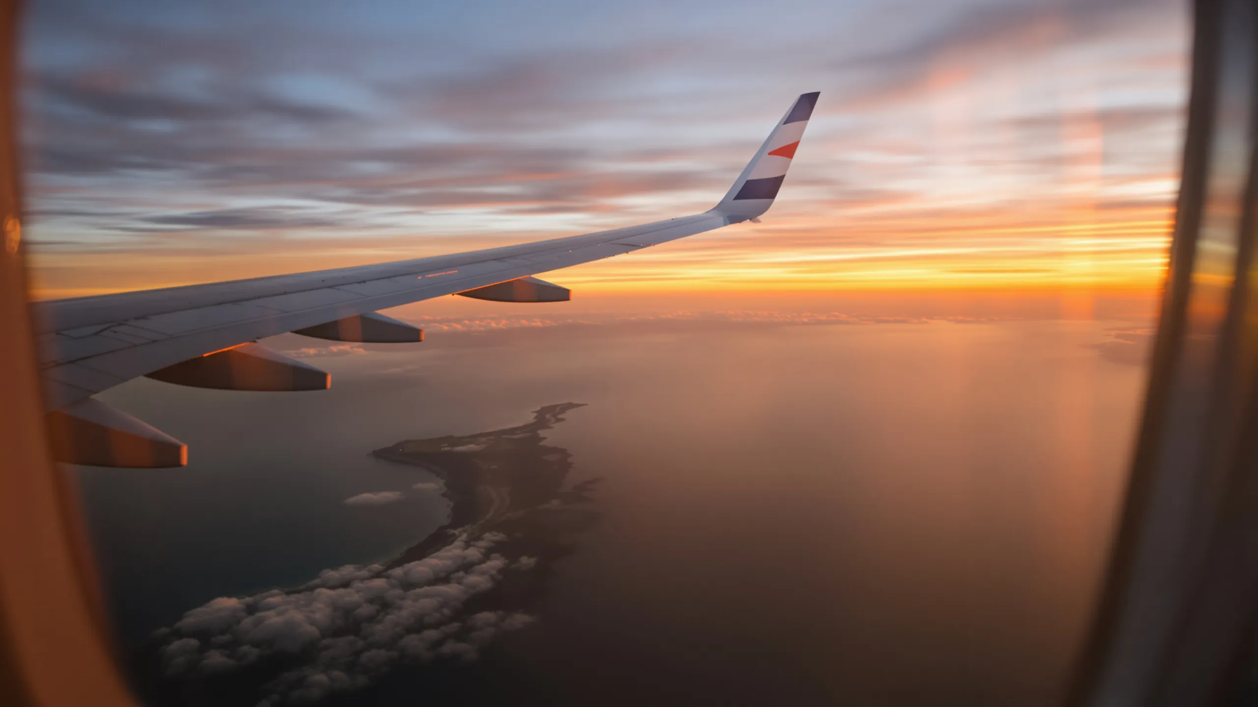 Blick aus dem Flugzeugfenster auf die Tragfläche und eine Küste bei Sonnenuntergang