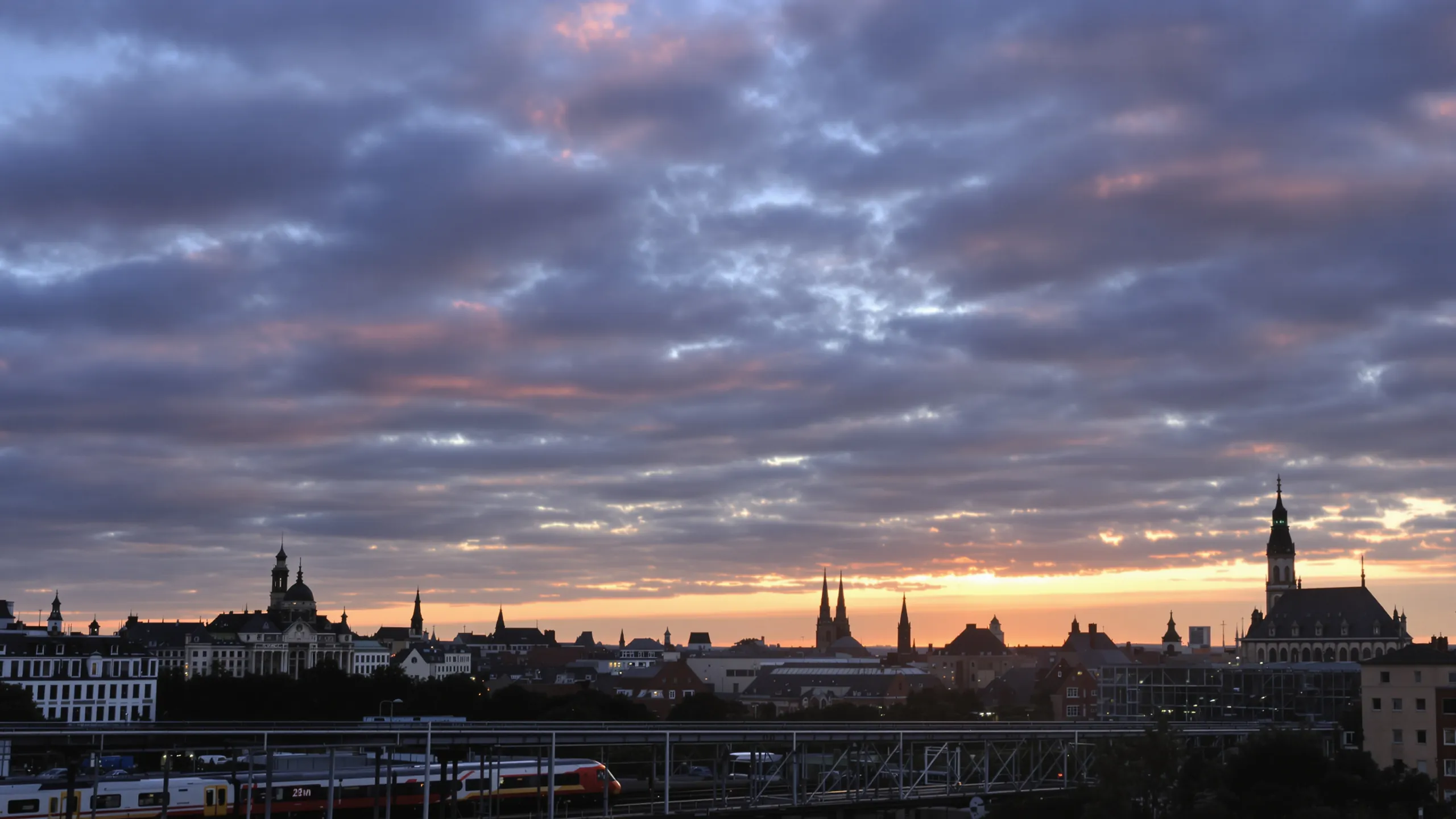 Stadtsilhouette einer belgischen Stadt mit Kirchtürmen unter dramatischem Abendhimmel