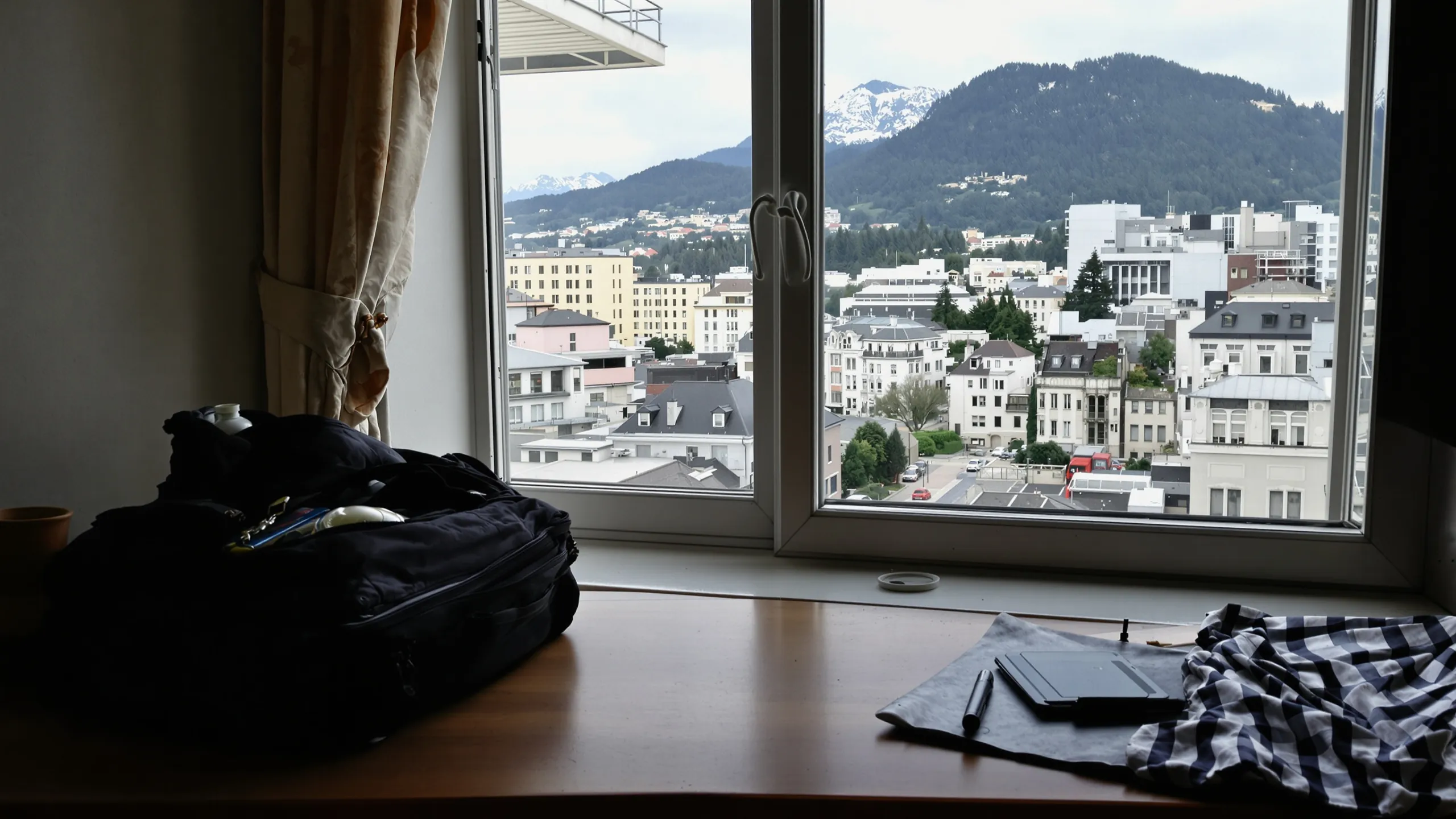 Gepackte Reisetasche am Fenster eines Apartments mit Blick auf eine Stadt am Hang