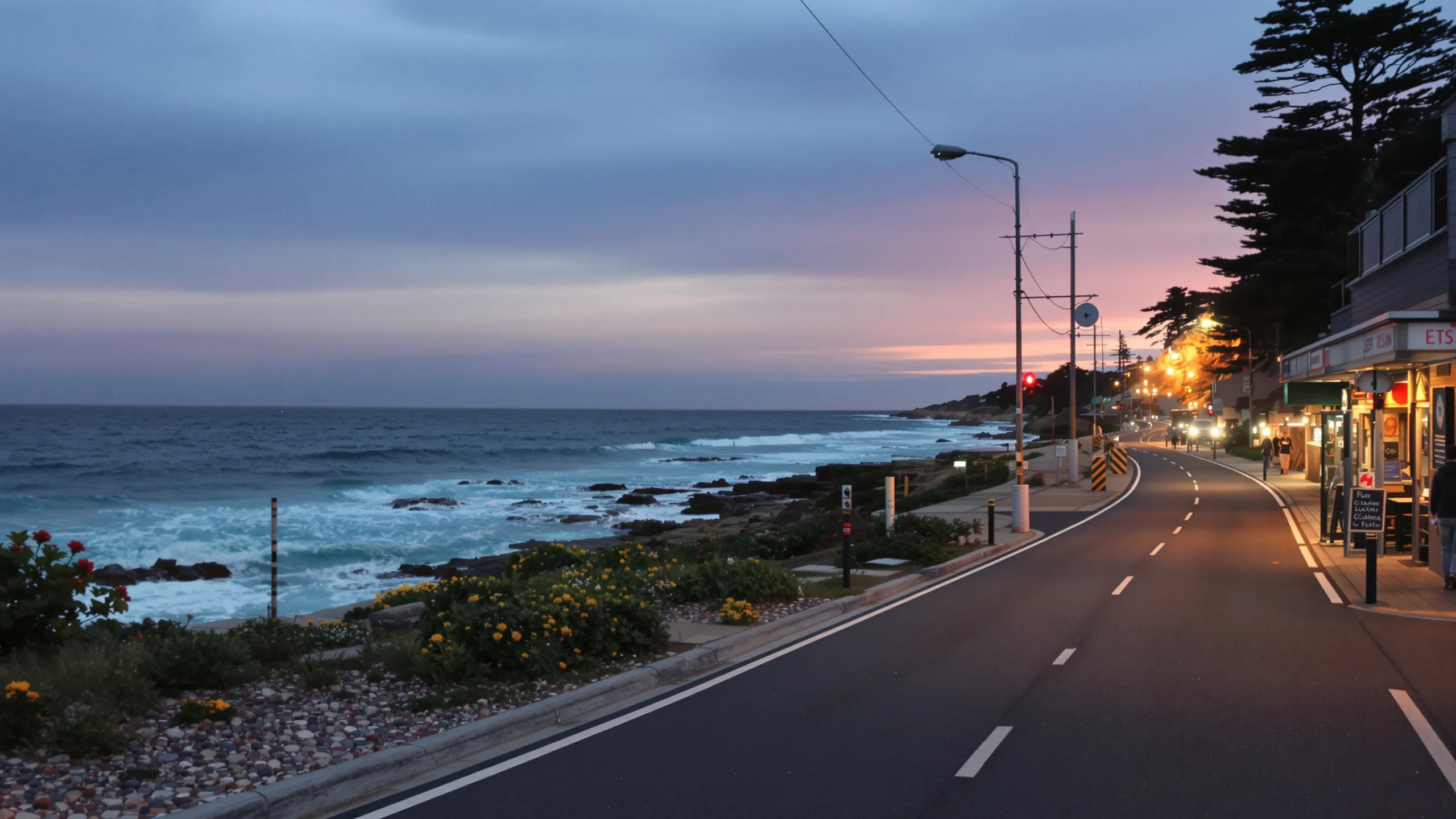 Küstenstraße in der Dämmerung mit Meer und beleuchteten Läden