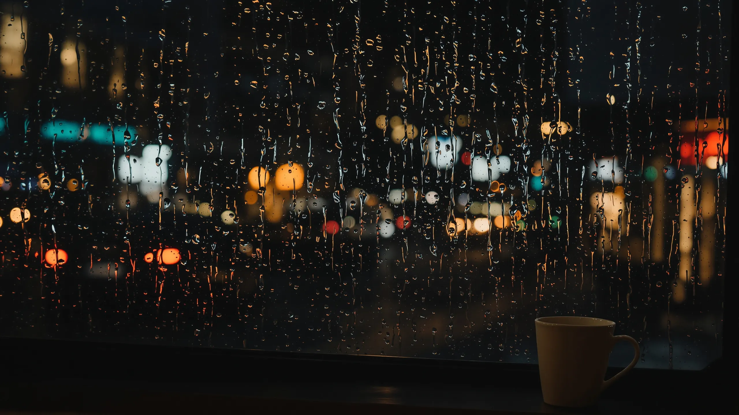 Regennasses Fenster bei Nacht mit verschwommenen Stadtlichtern und einer Tasse
