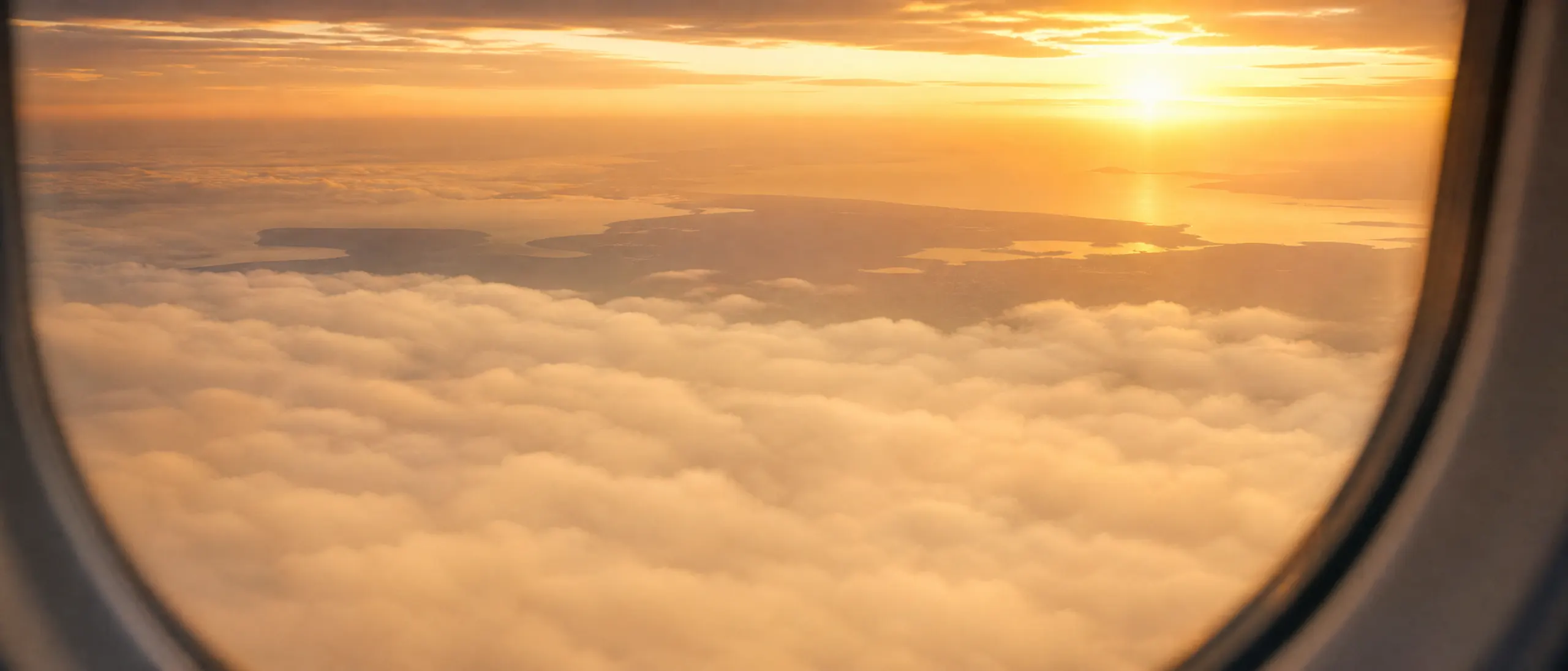 Blick über eine Wolkendecke im Morgenlicht auf eine ferne Küstenlinie