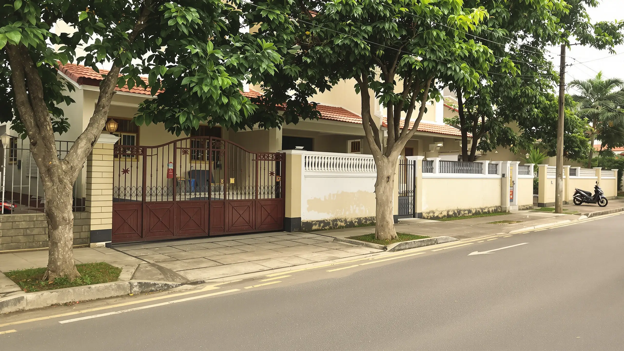 Ruhige Wohnstraße in Davao City mit Bäumen, Toreinfahrten und geparktem Motorrad im Alltagslicht